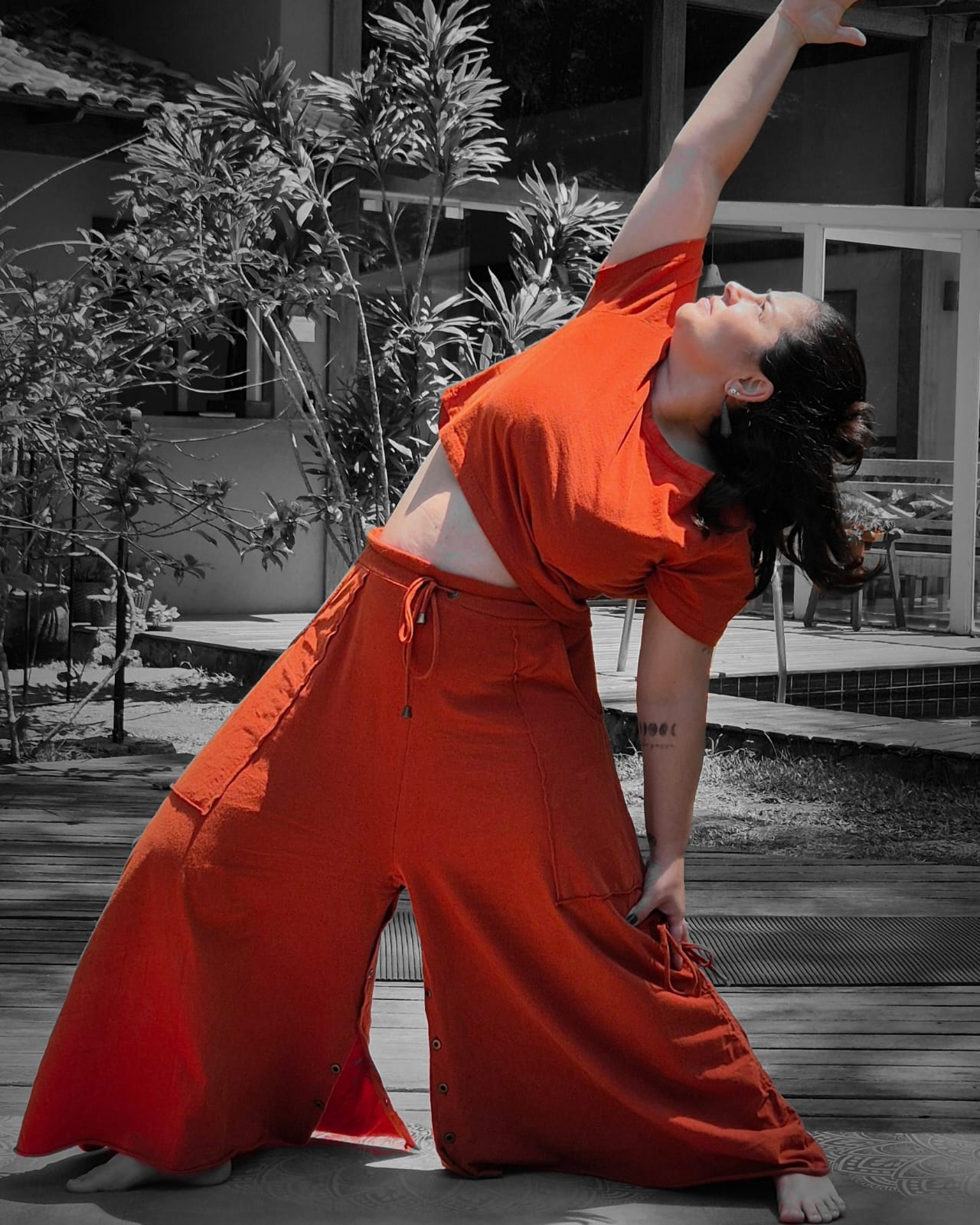 Raquel Fernandes em postura de yoga, roupa laranja terracota, braço estendido ao alto